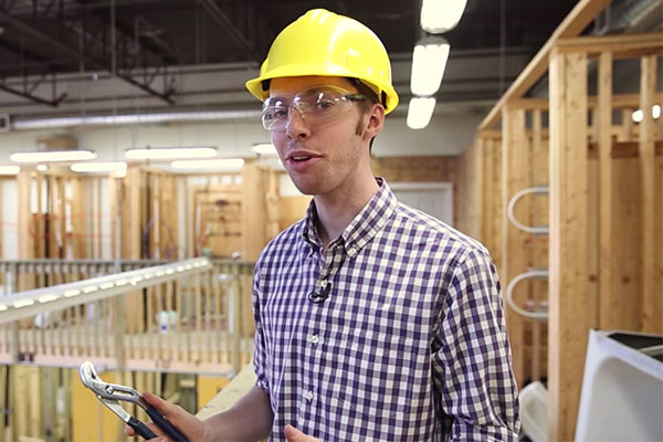 Student in the electrical lab holding pliers wearing a safety helmet and goggles