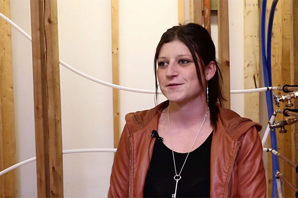 student standing in a plumbing shop with wooden fixtures and tubes leading to faucets in the background