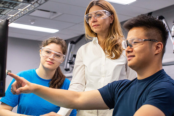 two students and a teacher looking at a computer screen