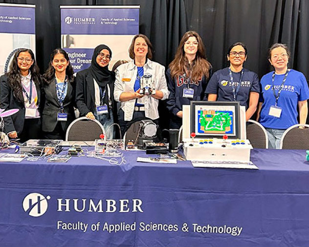 A group of people stands behind a Humber College tech display table