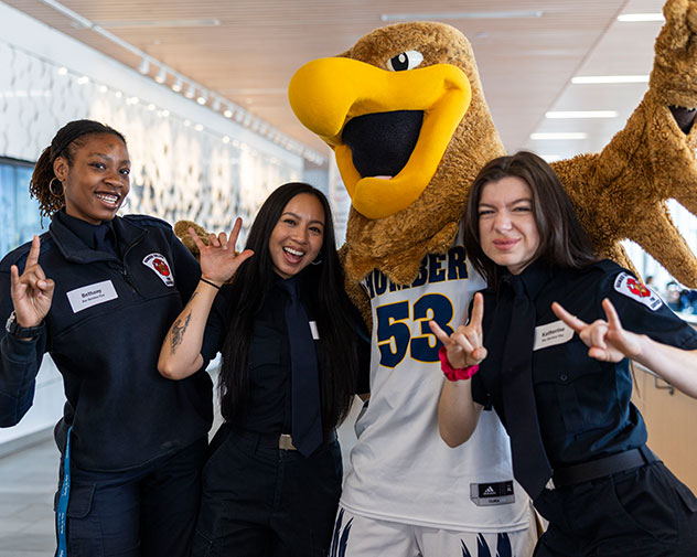 three students taking a photo with Howie the hawk