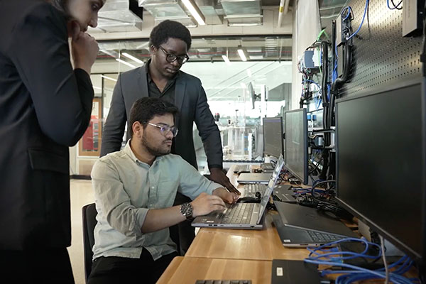 three people looking at a wall of computers