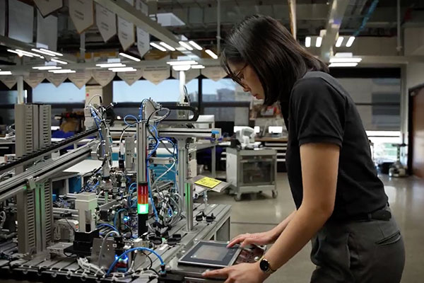 A person operates a control panel next to an automated machine in a modern industrial workspace.