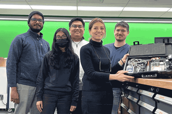 a professor is holding a black case filled with electronic instruments and joined by her research colleagues working on a research project