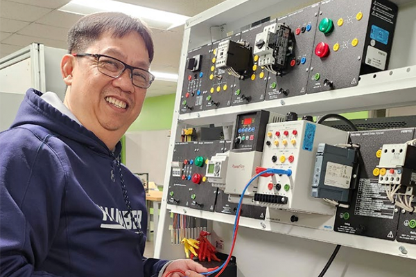 A skilled trades faculty member is smiling at the camera while working with electrical equipment