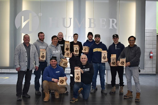 A group of faculty and students holding wooden birdhouses and smiling at the camera