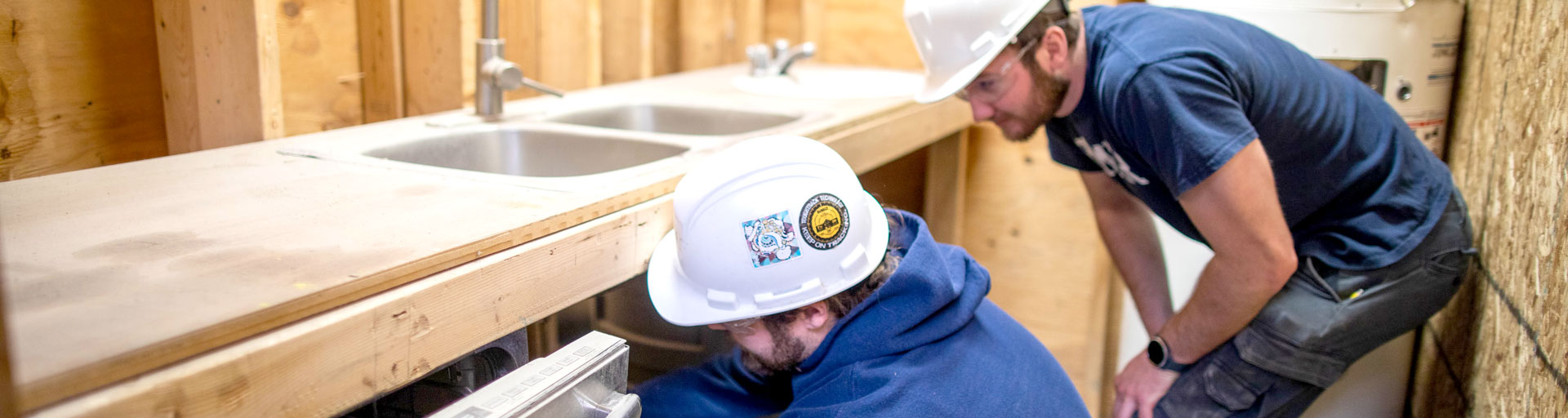 Two students in hard hats working on practice sink