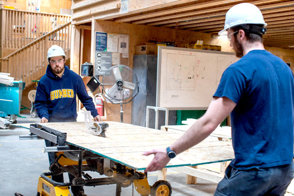 Two students holding a board over table saw