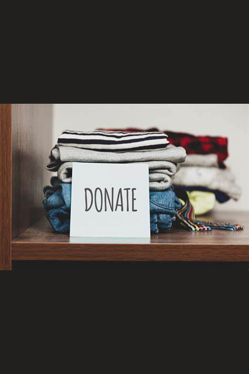 Folded up clothes on a shelf with a card that says "Donate" in front